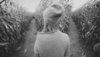 Black and white image of woman deciding between two paths in a corn maze
